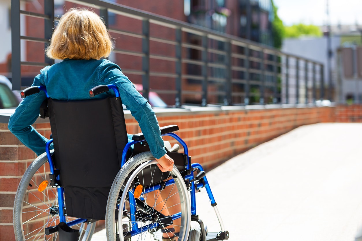 adult woman on wheelchair entering the platform or driveway - view from back